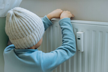 child warming hands over heater. Energy crisis in Europe