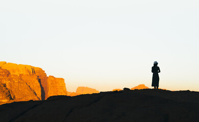 Silhouette of tourist woman on cliff greet sunrise in Jordan desert of Wadi Rum
