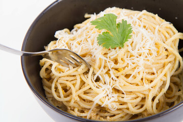 Yellow pepper pesto spaghetti covered with grated mozzarella cheese decorated with coriander being rolled around a fork - 542682798