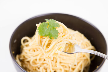 Yellow pepper pesto spaghetti covered with grated mozzarella cheese decorated with coriander being rolled around a fork