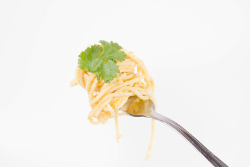 Yellow pepper pesto spaghetti covered with grated mozzarella cheese decorated with coriander rolled around a fork