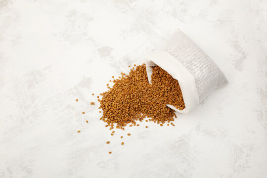 Fenugreek seeds spilled out of white pouch. Shambhala or helba is traditional Indian seasoning and ingredient Ayurvedic food. Trigonella foenum-graecum used in culinary and alternative medicine