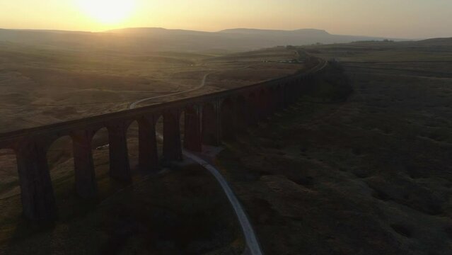 Aerial Drone Shot into Sun of Ribblehead Viaduct Train Bridge at Stunning Sunrise in Summer in Yorkshire Dales England UK with Hills in Background