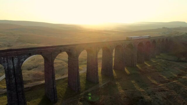 Aerial Drone Shot of Train travelling on Ribblehead Viaduct Train Bridge at Stunning Sunrise in Summer in Yorkshire Dales England UK with Hills in Background