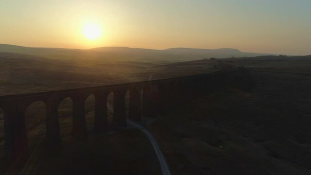 Aerial Drone Shot Into Sun Pulling back From Ribblehead Viaduct Train Bridge at Stunning Sunrise in Summer in Yorkshire Dales England UK with Hills in Background