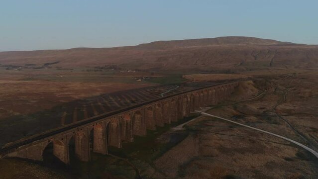 Aerial Drone Shot Pulling Back from Ribblehead Viaduct Train Bridgewith Long Shadow at Stunning Sunrise in Summer in Yorkshire Dales England UK with 3 Peaks Whernside Mountain in Background