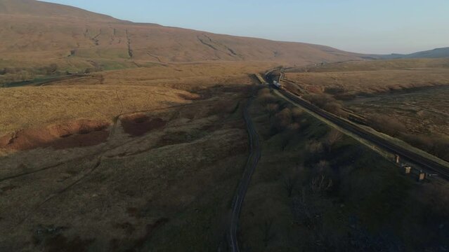 Aerial Drone Shot Following Train on Ribblehead Viaduct Train Bridge at Stunning Sunrise in Summer in Yorkshire Dales England UK Panning to 3 Peaks Whernside Mountain
