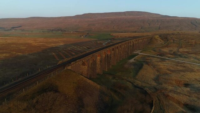 Slow Aerial Drone Shot of Ribblehead Viaduct Train Bridge with Long Shadows at Stunning Sunrise in Summer in Yorkshire Dales England UK with 3 Peaks Whernside Mountain in Background
