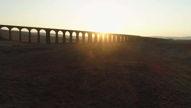 Low Aerial Drone Shot Rising Towards Silhouetted Ribblehead Viaduct Train Bridge at Stunning Sunrise in Summer in Yorkshire Dales England UK