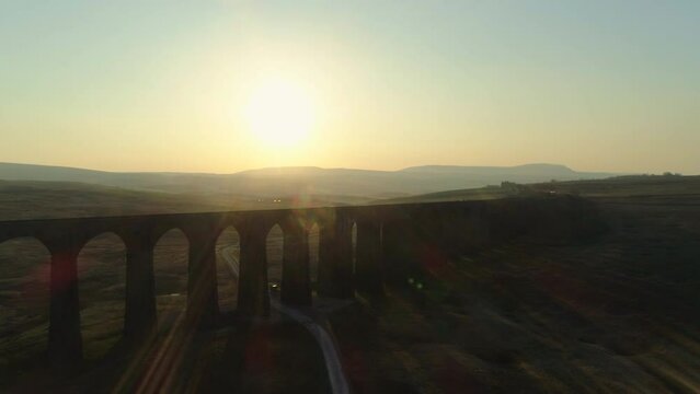 Aerial Drone Shot Rising Above Silhouetted Ribblehead Viaduct Train Bridge at Stunning Sunrise in Summer in Yorkshire Dales England UK with Hills in the Background