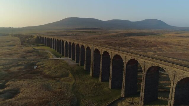 Low Aerial Drone Shot Closeup to Ribblehead Viaduct Train Bridge at Stunning Sunrise in Summer in Yorkshire Dales England UK with 3 Peaks Ingleborough Mountain in Background
