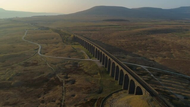 High Aerial Drone Shot Rotating Around Ribblehead Viaduct Train Bridge at Stunning Sunrise in Summer in Yorkshire Dales England UK with Ingleborough in background