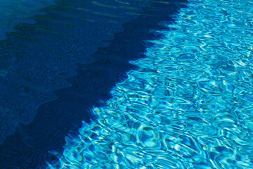 Two colored light and dark blue water with ripples and sunny reflections in swimming pool.