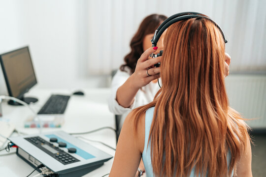 Audiologist doing impedance audiometry or diagnosis of hearing impairment. An beautiful redhead adult woman getting an auditory test at a hearing clinic.