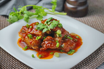Pork Ribs in Red Sauce served on a white plate in a restaurant.