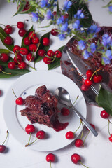 Chocolate cake with sweet cherry, cup of tea and bouquet of blue flowers on white background..