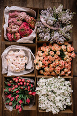 Many beautiful flower mono bouquets of fresh roses, ranunculus, lilac, matthiola, tulips, wrapped in paper, placed in a cardboard transportation box, close up view - 542687519