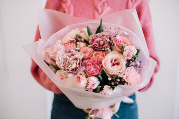Very nice young woman holding big and beautiful flower bouquet of fresh roses, carnations, ranunculus, tulip, baby breath flowers in pink colors, close up view