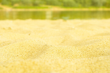 Sandy beach near the river with a forest on the other side. Close-up of sand in soft focus.