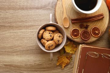 Obraz na płótnie Canvas Cup of tea or coffee, seasonal spices, bowl of cookies, blanket, pumpkins, colorful leaves, books and tangerines on wooden table. Cozy hygge at home. Top view.