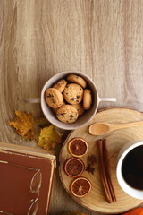 Fototapeta na wymiar Cup of tea or coffee, seasonal spices, bowl of cookies, blanket, pumpkins, colorful leaves, books and tangerines on wooden table. Cozy hygge at home. Top view.