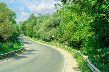 Fototapeta premium Asphalt two-lane road in the countryside surrounded by trees. Route turn.