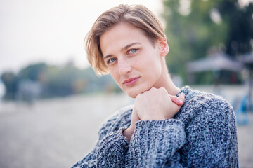 Portrait of a young elegant stylish blonde woman with a short haircut in a sweater. Looking at the camera with a smile, hands to her face