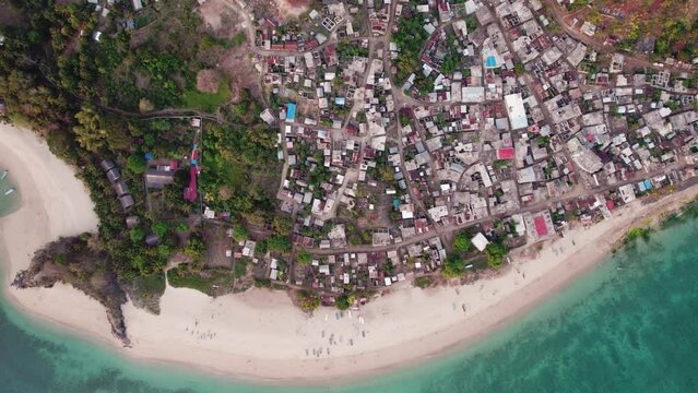 Aerial of small village town in Comoros, next to sand beach and blue water, zoom in