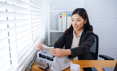 Asian accountant businesswoman using banknote counter machine counting money bill cash in office,...