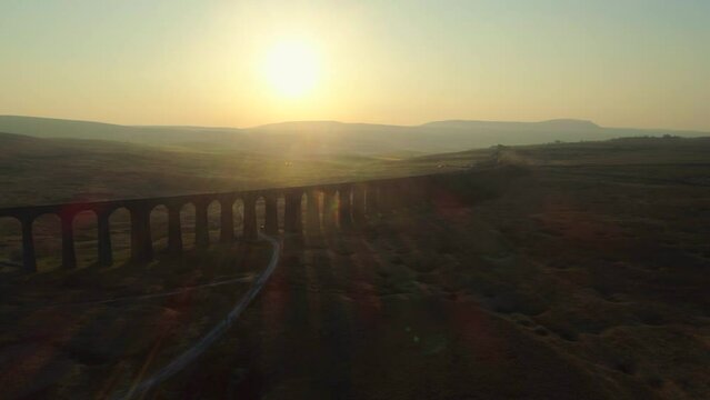 Aerial Drone Shot of Silhouetted Ribblehead Viaduct Train Bridge at Stunning Sunrise in Summer in Yorkshire Dales England UK with Hills in Background