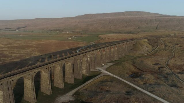 Aerial Drone Shot Pulling Back from Ribblehead Viaduct Train Bridge at Stunning Sunrise with Long Shadows in Summer in Yorkshire Dales England UK with 3 Peaks Whernside Mountain in Background