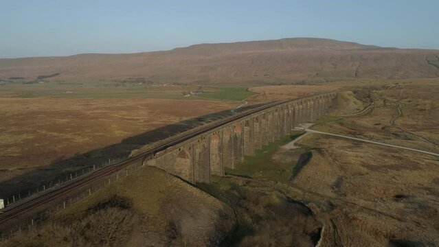 Aerial Drone Shot Pulling away from Ribblehead Viaduct Train Bridge at Stunning Sunrise in Summer in Yorkshire Dales England UK with 3 peaks Whernside mountain in background