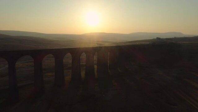 Aerial Drone Shot Pulling Back From Ribblehead Viaduct Train Bridge at Stunning Sunrise in Summer in Yorkshire Dales England UK with Hills in Background