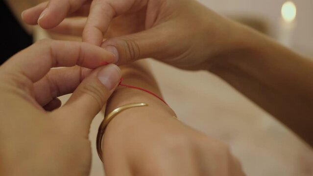 Religious ritual close up. Female hands tie a red thread around the woman's wrist as a blessing for good luck and peace