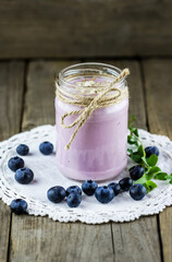 Glass jar of handmade blueberry yogurt with fresh blueberries on old wooden background