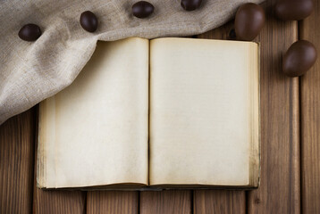 Top view of blank old book with vintage pages and chocolate eggs in the sackcloth on wooden background