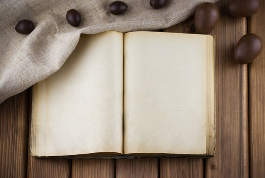 Top view of blank old book with vintage pages and chocolate eggs in the sackcloth on wooden background