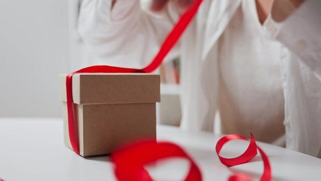 Opening a gift with a red ribbon female hands open a gift on a holiday taking off a gift box red ribbon bow. new year valentine's day christmas wedding anniversary
