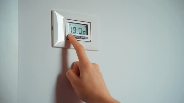 Hand putting down degrees. Girl feeling cold with home heating trouble. Energy crisis concept. Radiator thermostat showing cold temperature. Electricity and gas bill goes up. Radiators turns off.