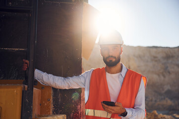 With smartphone in hands. Beautiful sunlight. Man in uniform is working in the quarry at daytime © standret