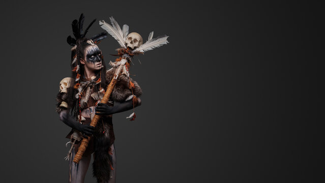 Studio shot of fearful witch woman dressed in plumed attire holding staff.