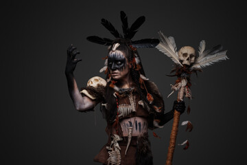 Studio shot of dark voodoo witch with painted face holding staff.
