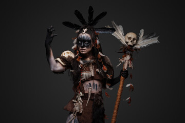 Portrait of spooky voodoo witch dressed in dark clothes holding staff with skull. - obrazy, fototapety, plakaty