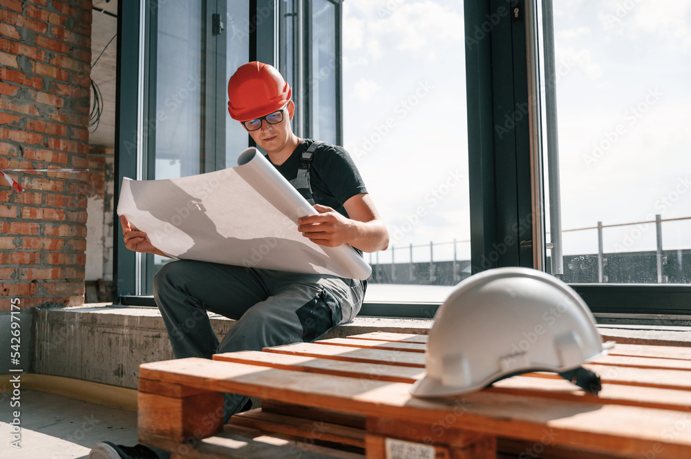 Wall mural foreman in hard hat is sitting indoors and reading plan of the building and construction