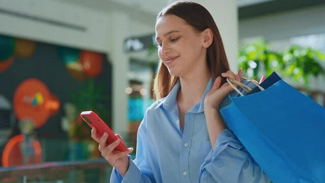 Smiled female customer using smartphone amd holding her purchase in the paper bags. Woman carrying her shopping-bags , using her phone. Young lady chattinh with friends after shopping