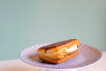 Pastry with chocolate and pudding on plate in bakery against green wall