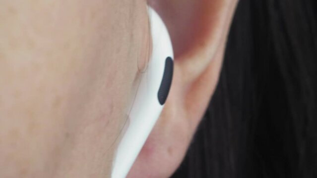 The girl puts a white wireless earpiece in her ear. Female ear close-up. macro video.