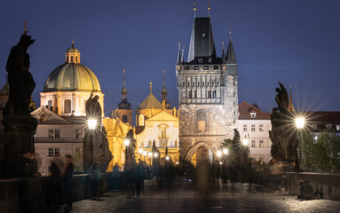 People walking on busy historical Charles bridge during late evening, Prague, Czechia