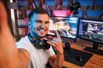 Making selfie, celebrating victory. Male game streamer in casual clothes is indoors with pc