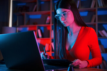 Young female retoucher working with computer and graphic tablet in neon lighting office